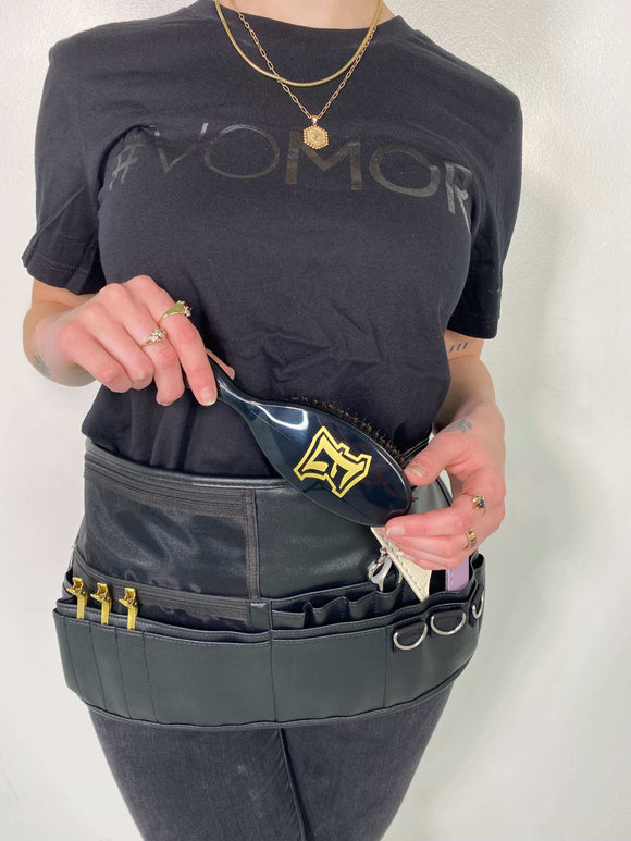Person wearing a black shirt and Aveda Arts Tool Belt holding a brush, showcasing convenient tool storage for stylists and makeup artists.