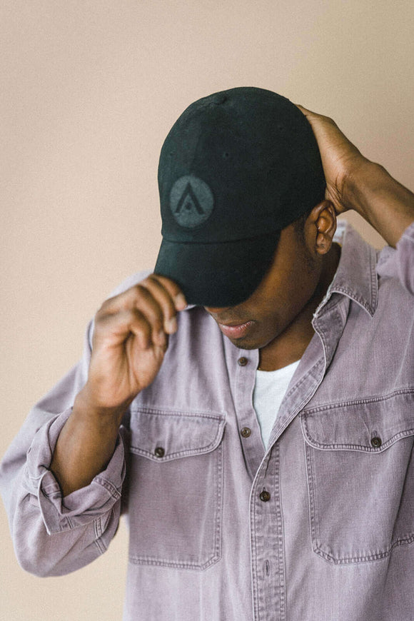 Man wearing black Aveda Arts baseball cap with embroidered logo and adjustable back