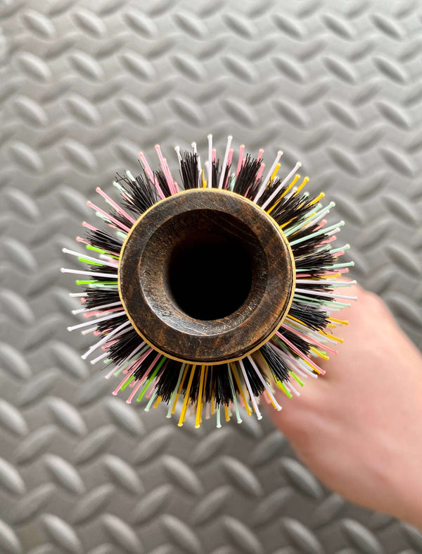 Top view of ElevateHair Rainbow Thermal Brush with colorful nylon and natural boar bristles, held in hand on a patterned background
