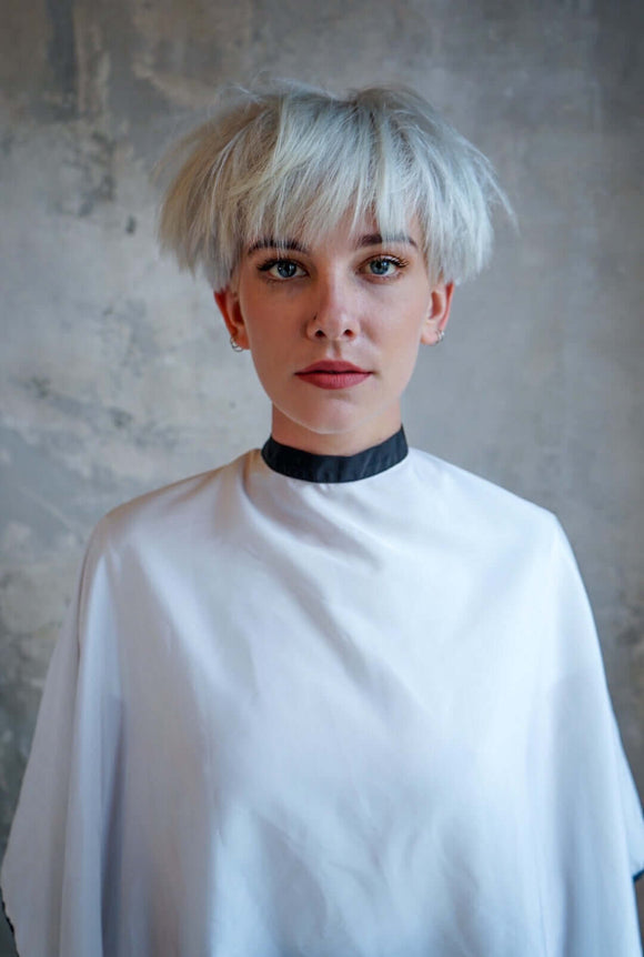 Woman wearing Elevate Hair White Cape with black collar standing against a gray textured background