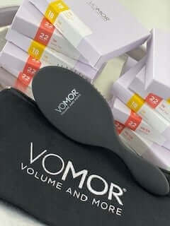 VoMor Detangling Brush displayed with boxes of hair extensions and carrying pouch.