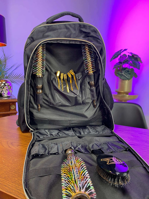 E Stylist Barber Backpack with multiple pockets, open compartments, and tools for barbering, displayed on a wooden table in a vibrant background.